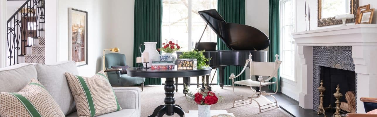 A living room with emerald green curtains, a sleek black piano, and roses on a table