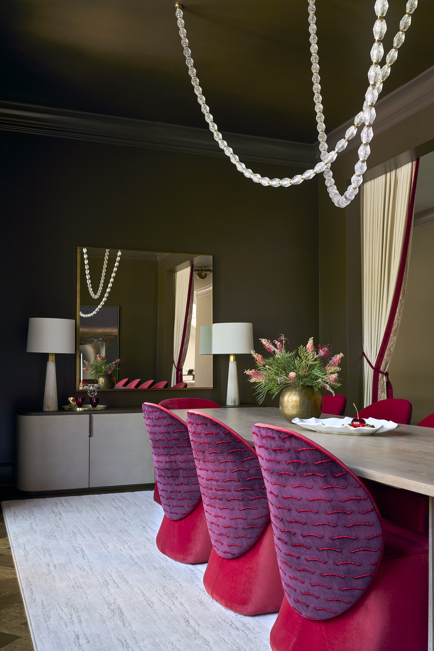 A richly colored and textured dining room with fashion-forward purple and red chairs, draped lighting, and dark walls