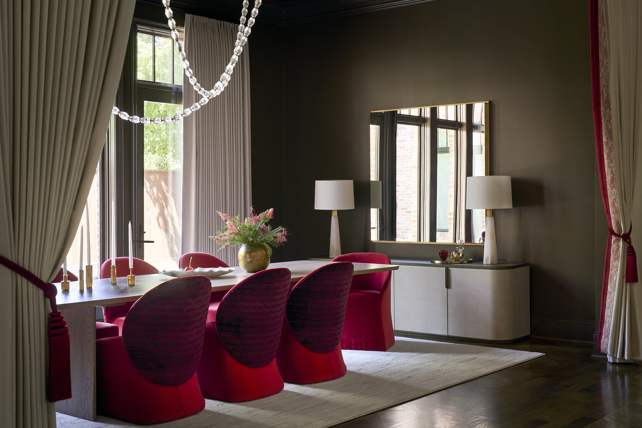 A richly colored and textured dining room with fashion-forward purple and red chairs, draped lighting, and dark walls