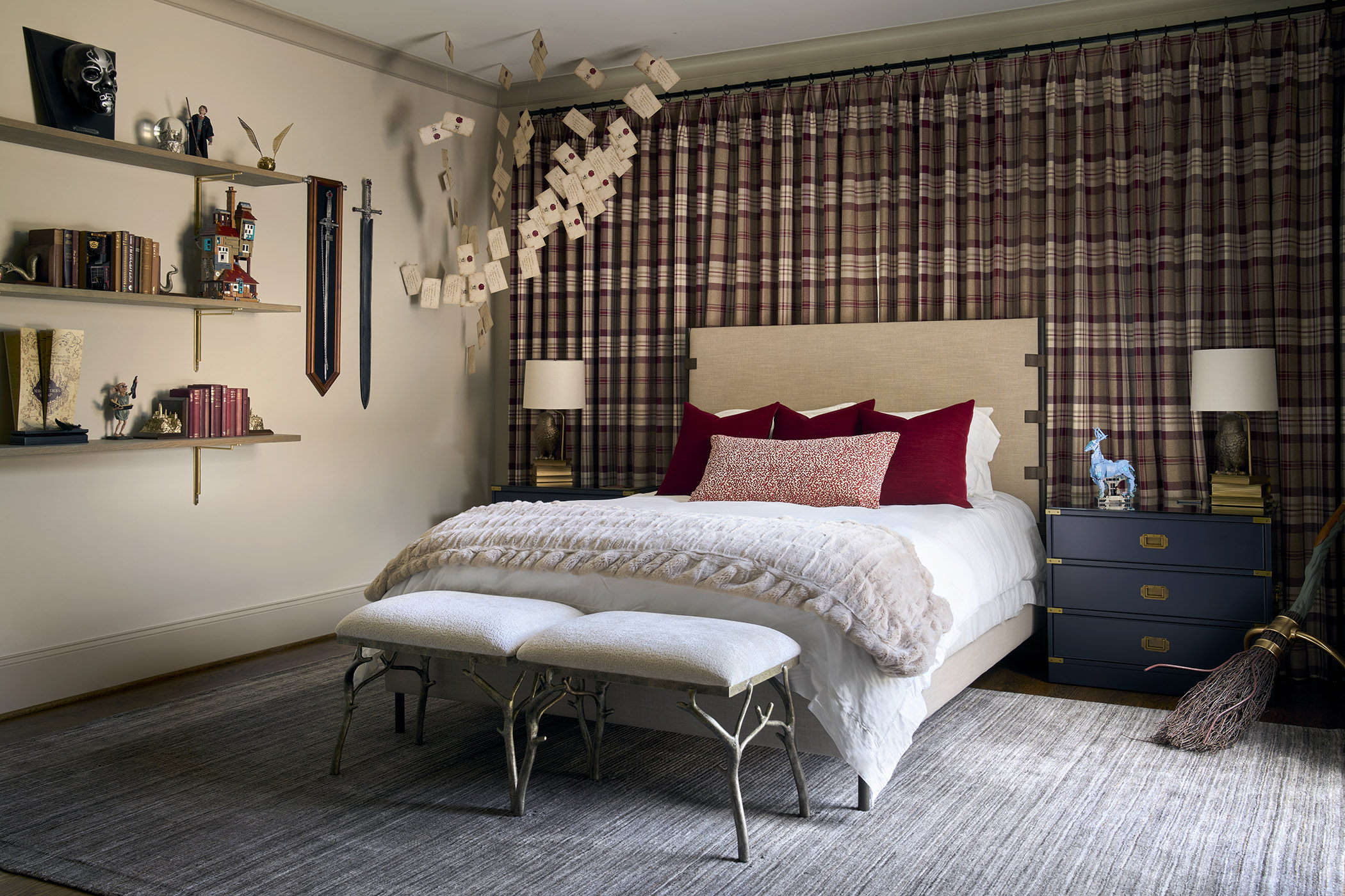 Harry Potter-inspired guest bedroom with plaid wall-to-wall drapery, burgundy pillows, navy nightstands, floating letters, collectibles, and a broom.
