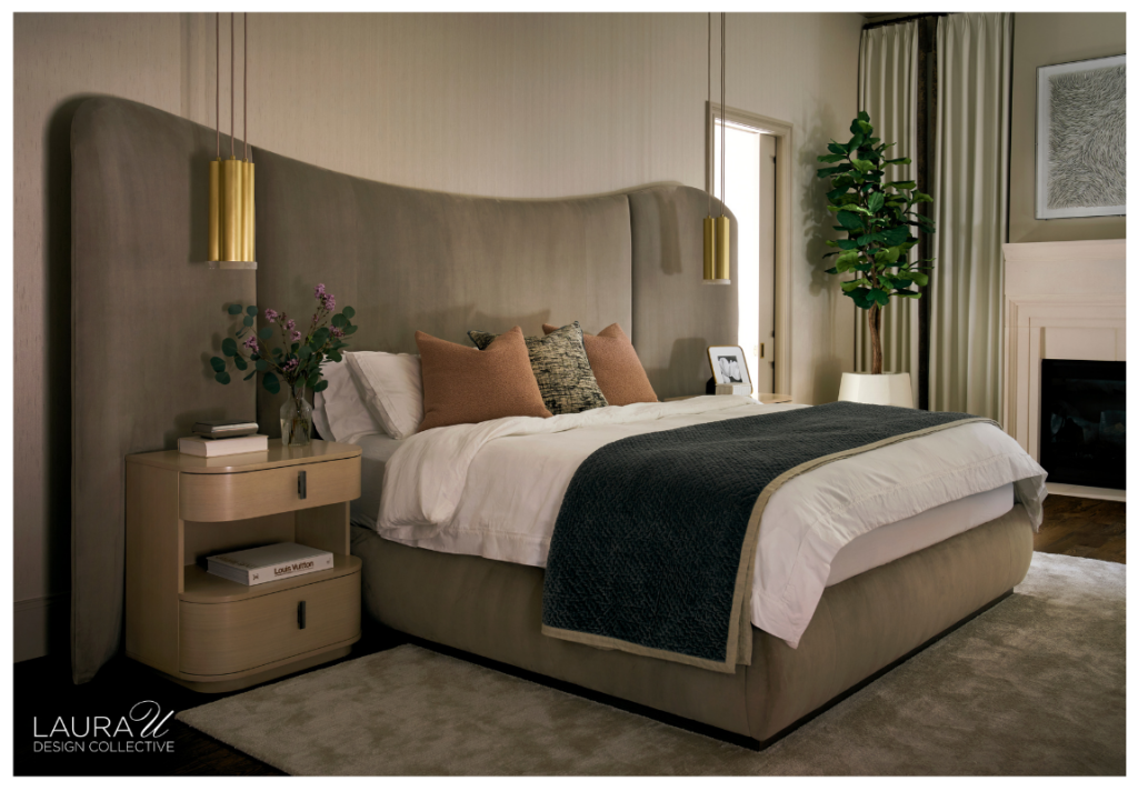 Primary bedroom with an oversized curved taupe headboard, brass pendant lights, rounded nightstands, white bedding, a dark blue throw, fireplace, and tall potted tree.