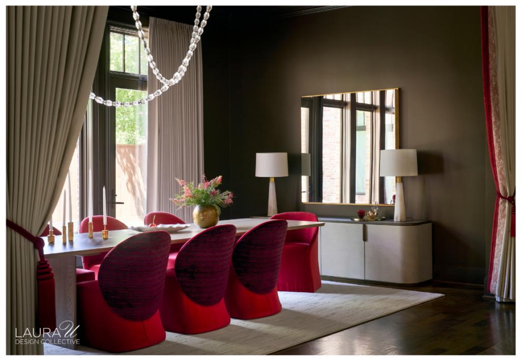 Wide view of the olive dining room with cherry-red sculptural chairs, a pale table and rug, looping glass chandelier, mirrored sideboard, and red-trimmed drapery.