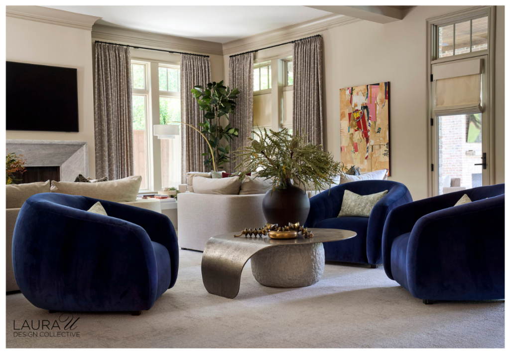 Spacious living room with pale sectional seating, colorful abstract art, textured gray drapery, white cocktail tables, patterned pillows, and lush greenery.