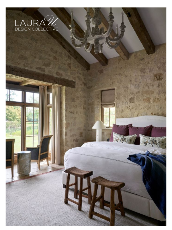 Rustic stone bedroom with white bedding, plum accent pillows, patterned decorative pillows, and wood furnishings.