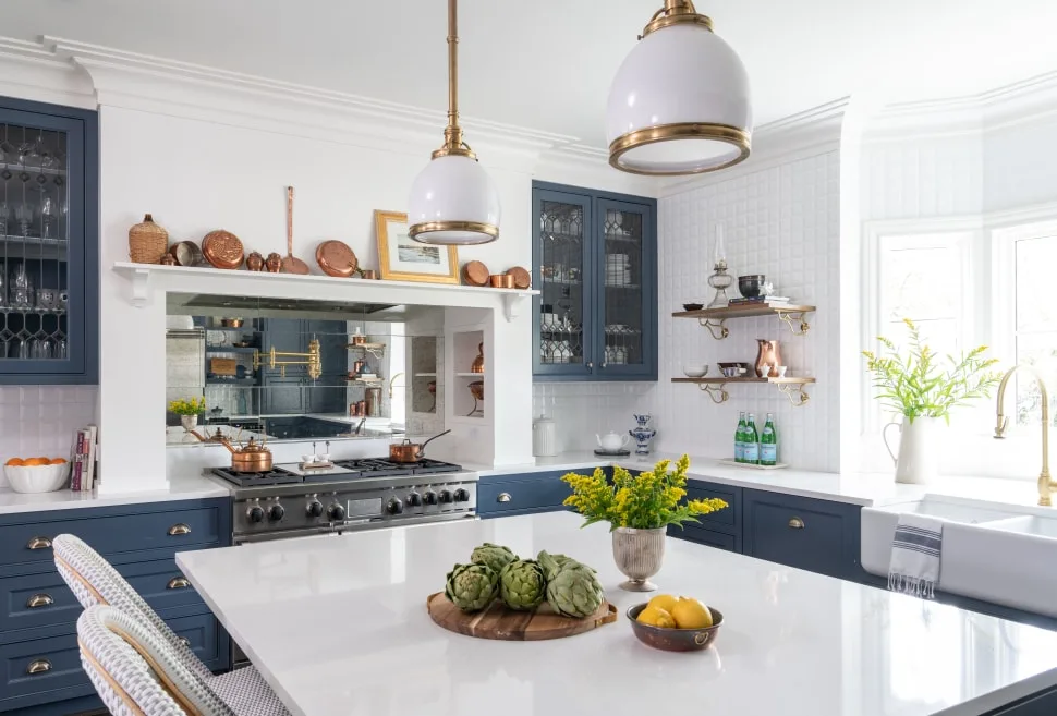 A brilliantly white and blue kitchen with apron sink, large island, and copper collection.