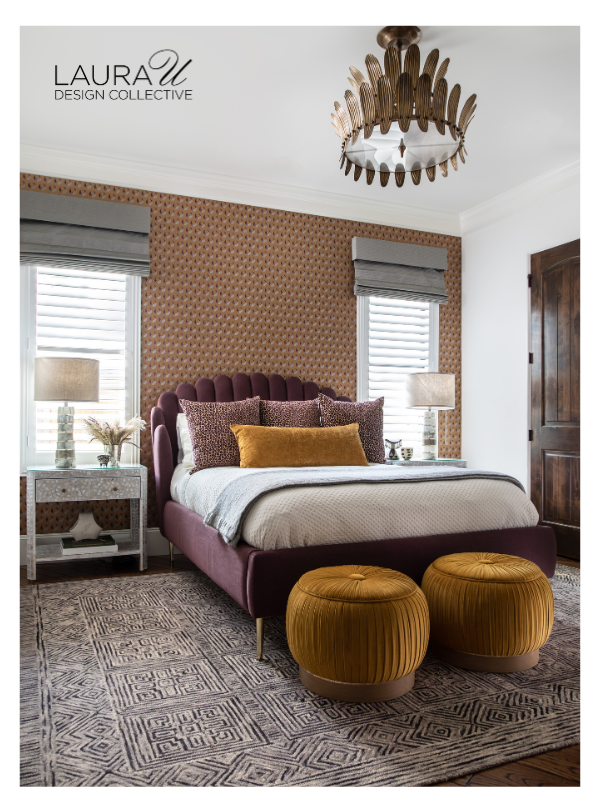 Plum upholstered bed with layered sleeping pillows, textured decorative pillows, and an ochre lumbar pillow in front of patterned wallpaper.