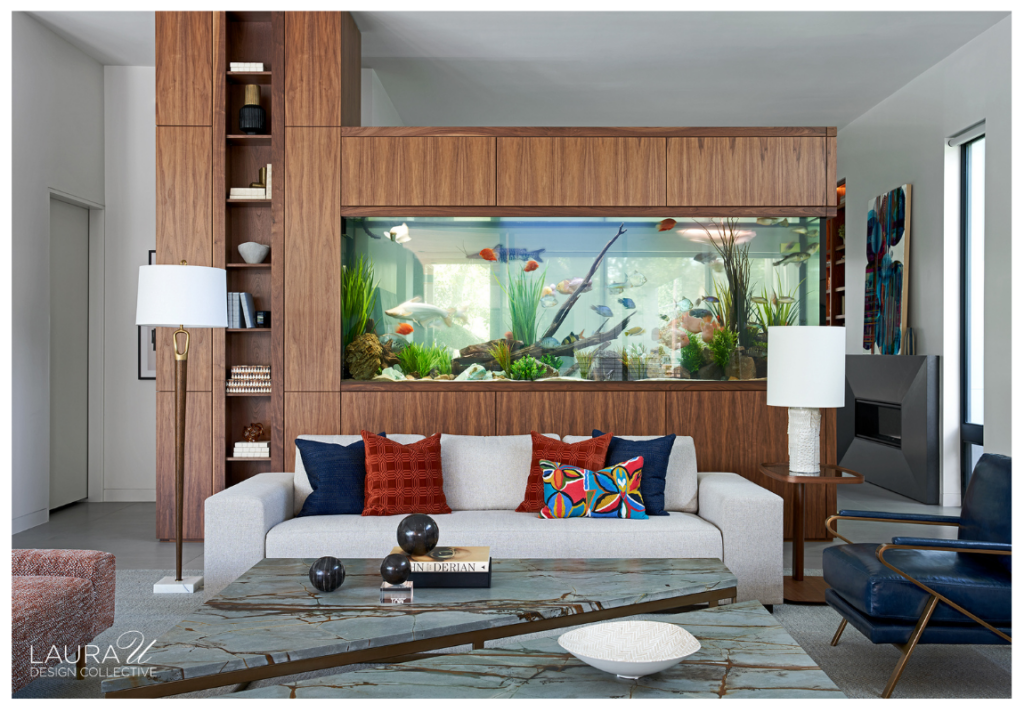Braeswood living room by Laura U Design Collective featuring a built-in aquarium framed by walnut cabinetry, a light gray sofa with colorful accent pillows, and a blue stone coffee table.