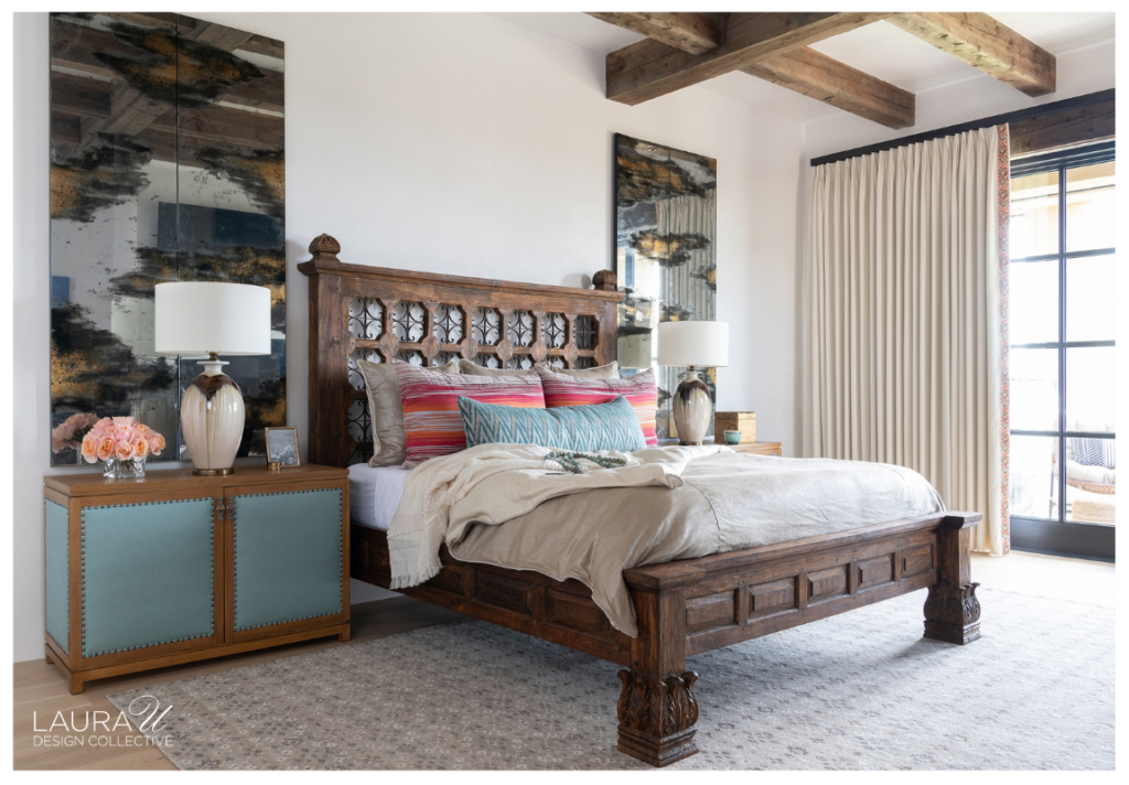 Camino Haciendas bedroom featuring an intricately carved wooden bed, blue upholstered bedside cabinets, colorful striped pillows, oversized abstract artwork, and rustic exposed ceiling beams.