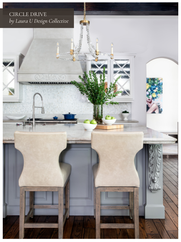 Elegant kitchen island with carved detailing, leather barstools, and a crystal chandelier overhead