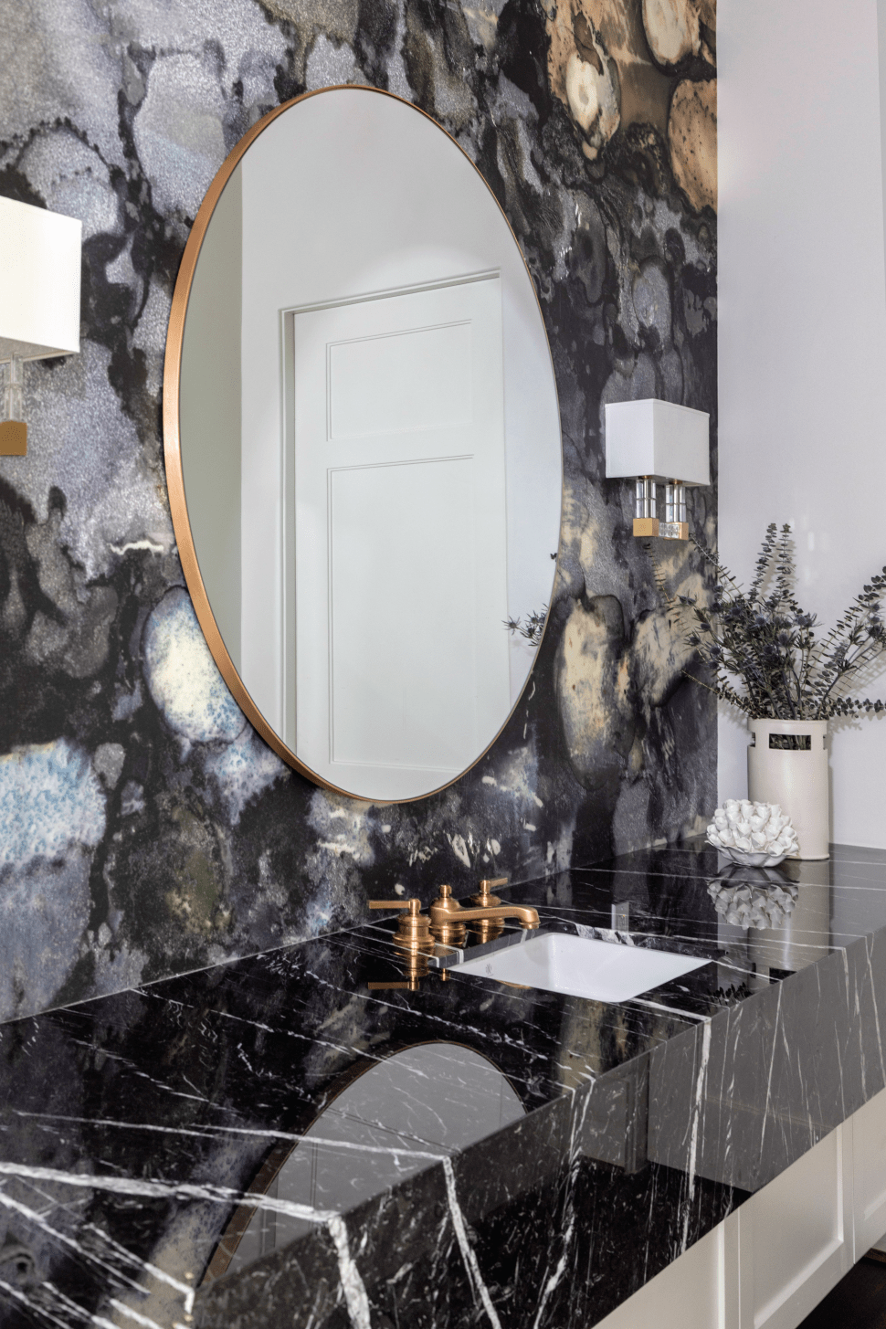 Dramatic powder bath with round mirror, black & white marble countertop and white cabinets .