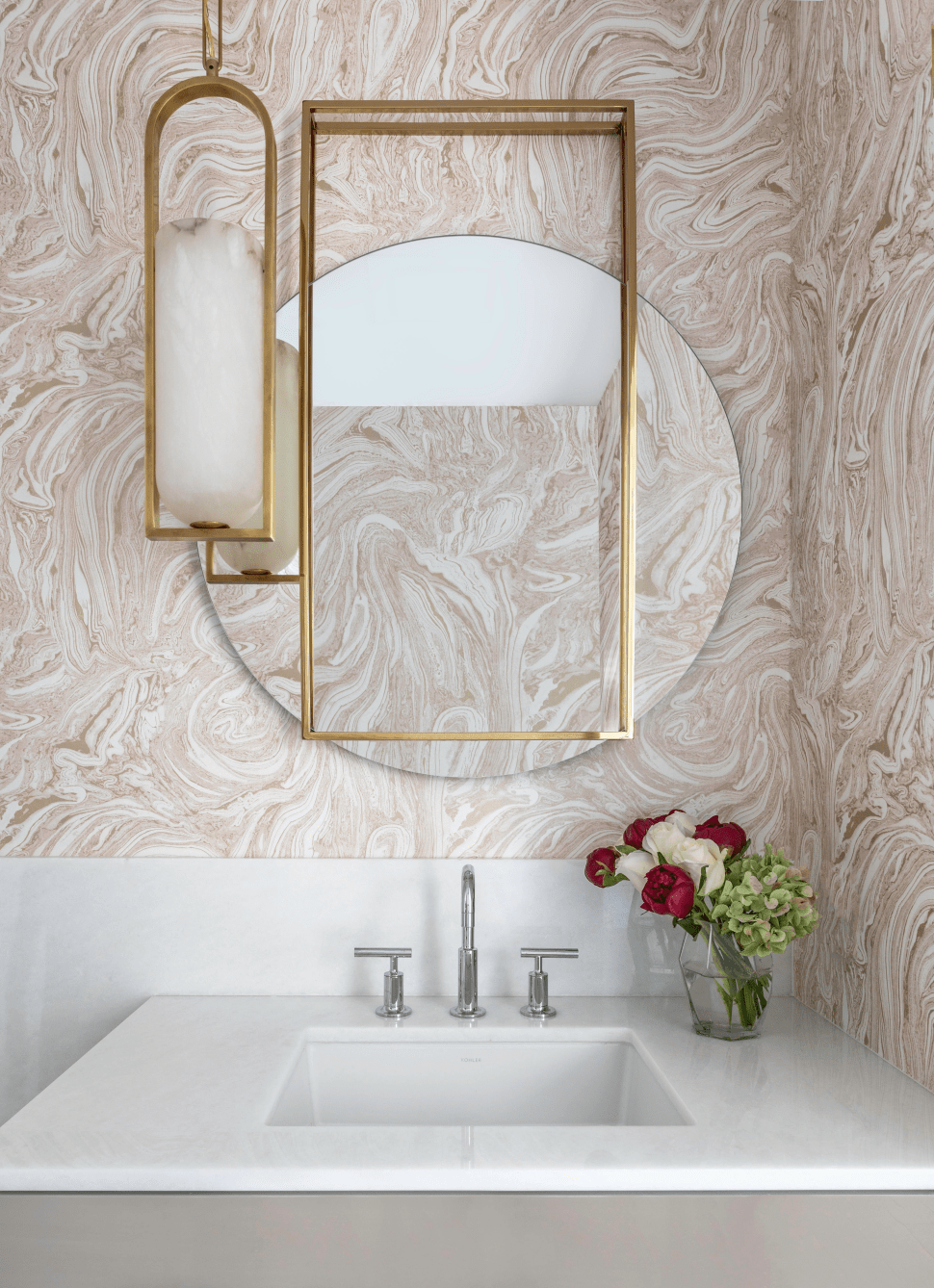 Elegant powder bath with round mirror, patterned wallpaper,  copper lights and mirror frame.