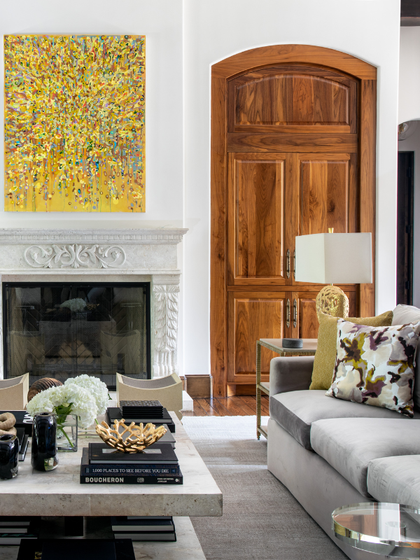 Living room anchored by a yellow abstract painting, carved fireplace, and tailored neutral seating