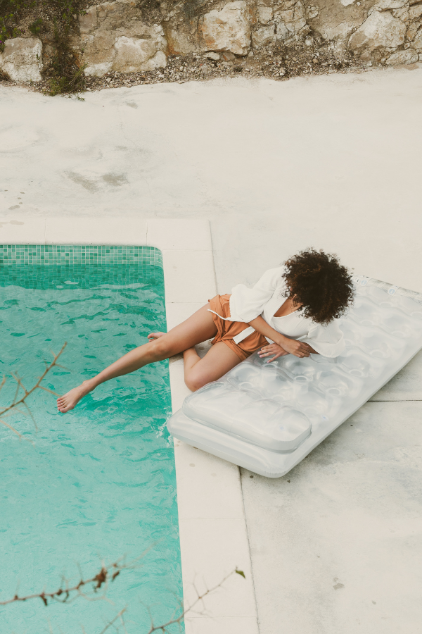 A woman dipping her toe in the pool while laying on a blow-up chaise with mosaic pool tile