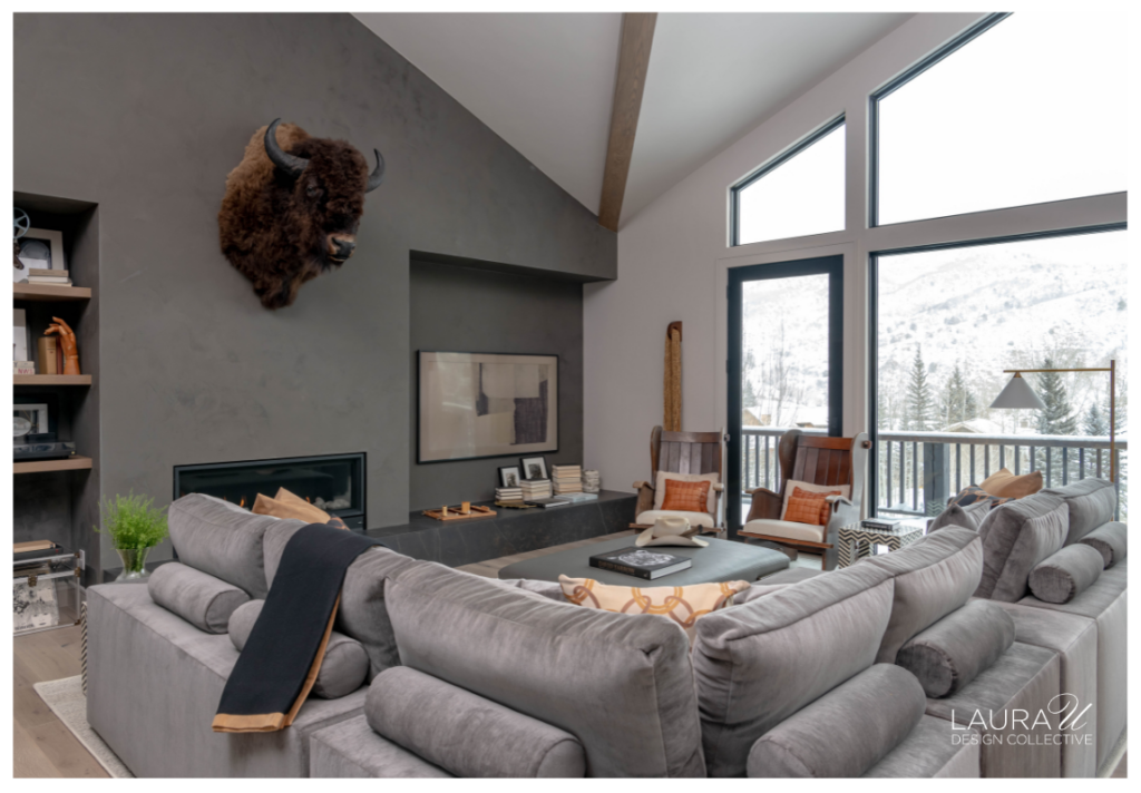 Aspen living room with a gray sectional, dark plaster fireplace wall, vaulted ceiling, and large windows overlooking snowy mountain views.