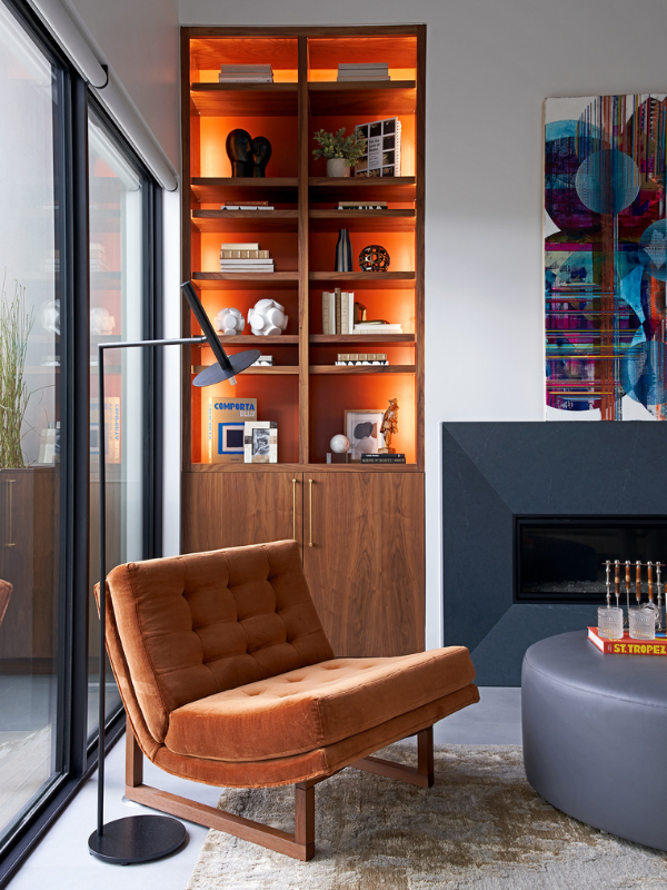 the living room in Braeswood Place with a glowing cabinet, orange chair, and steel blue accents